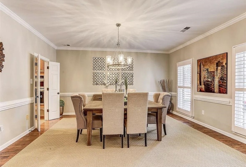 Formal dining area featuring a contemporary chandelier, crown molding, chair rail detailing, wood-finish flooring, and white plantation shutters
