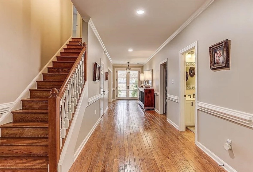 Foyer featuring wood-finish flooring, a grand staircase with white balusters, crown molding, chair rail molding, and a transom window above French doors