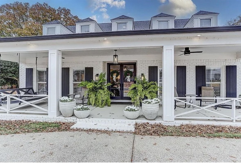White brick exterior with a deep covered porch, featuring black-framed double entry doors and coordinating black louvered shutters