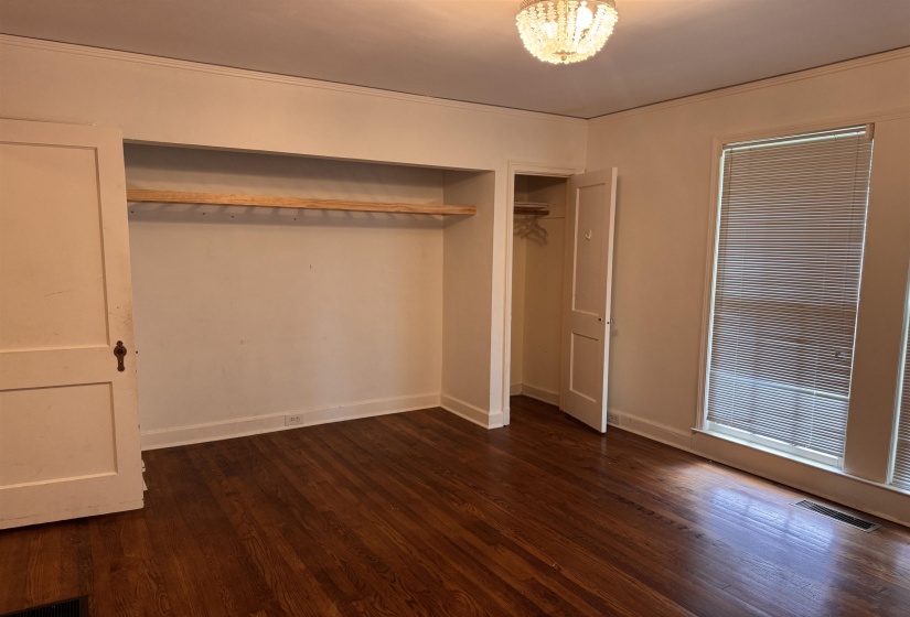 Hardwood flooring, recessed closet with hanging rod, additional closet, window with blinds, and a crystal chandelier