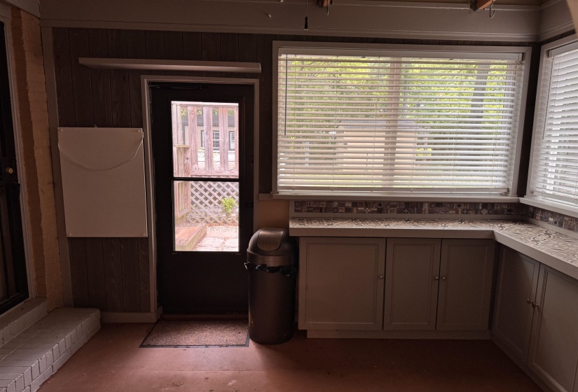 Enclosed sunroom featuring a paneled wall finish, corner built-in cabinetry with a patterned countertop, a decorative tile backsplash, and multiple windows with blinds