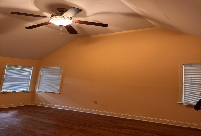 Room with vaulted ceiling, wood-finish flooring, and multiple windows with blinds