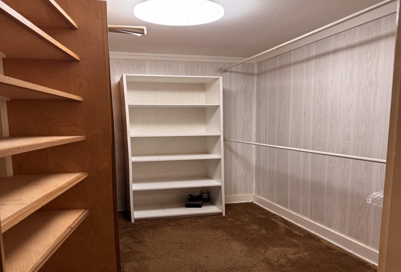 Walk-in closet with built-in wood shelving units, white built-in shelving, hanging rod, textured wall covering, and flush mount ceiling light