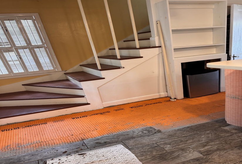 Staircase with wood treads and white risers, featuring built-in shelving, a mini-refrigerator, and a window with plantation shutters