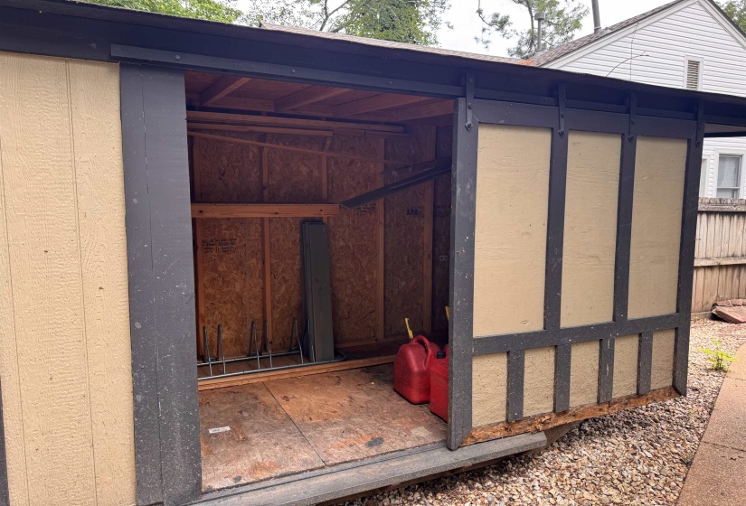 Detached storage shed featuring a tan and dark gray exterior, exposed wood interior framing, and a sliding barn door