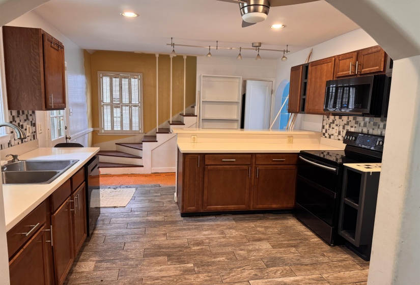 Kitchen featuring wood-finish flooring, wood cabinetry, light-toned countertops, a tile backsplash, and a stainless steel sink with a modern faucet