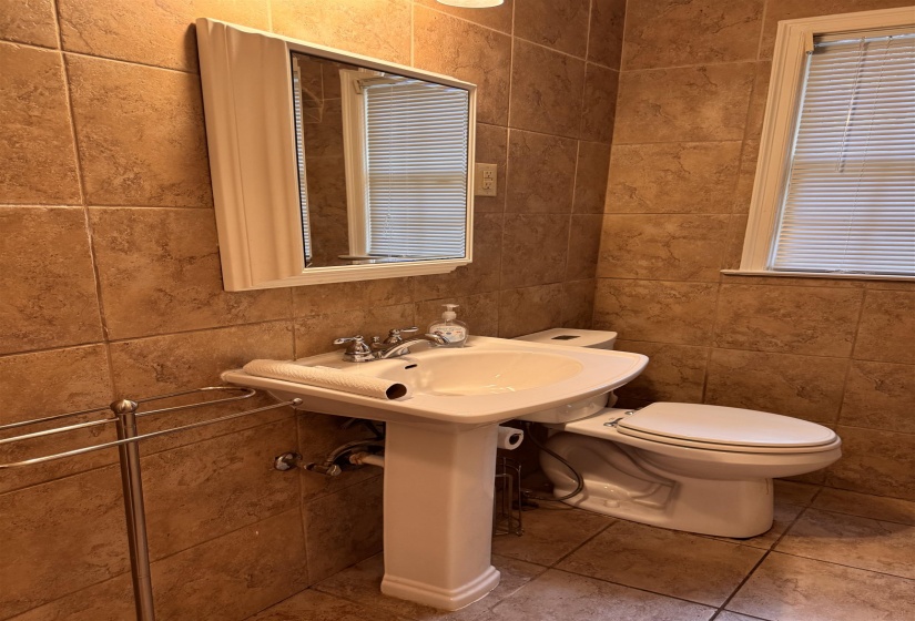 Bathroom featuring a pedestal sink, chrome faucet, and tiled walls extending to the floor