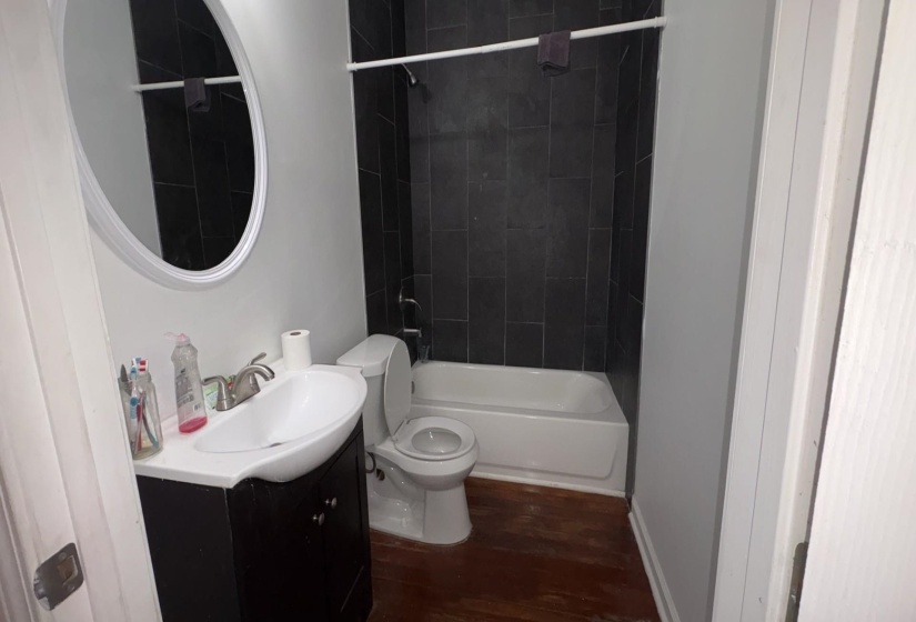 Bathroom featuring dark tiled shower surround, white bathtub, and wood-finish flooring