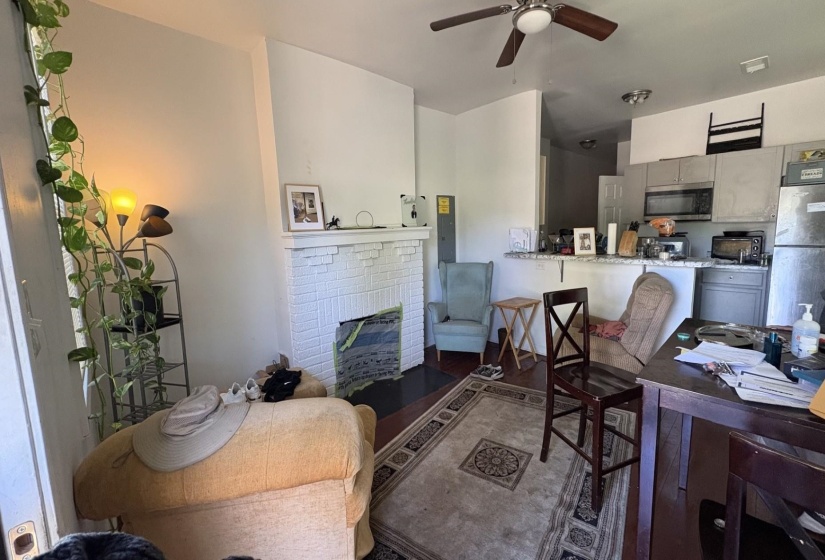 Living area featuring a white brick fireplace, dark wood-finish flooring, and a ceiling fan