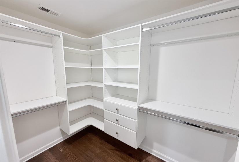 Walk in closet with custom cabinets and dark hardwood flooring