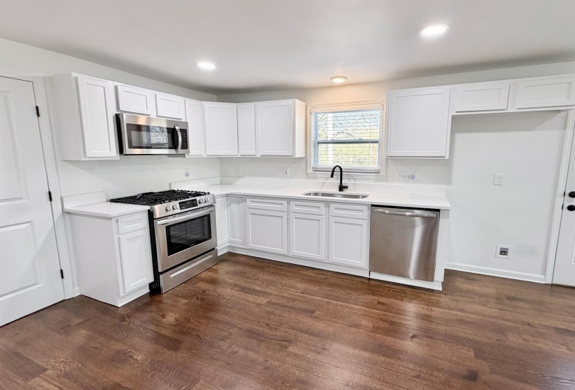 Kitchen with stainless steel appliances, white cabinets, quartz countertops, dark hardwood finished floors, and recessed lighting