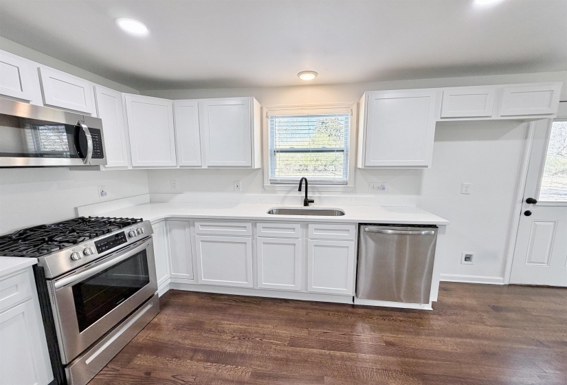 Kitchen featuring stainless steel appliances, white cabinetry, dark hardwood finished floors, light quartz countertops, and recessed lighting
