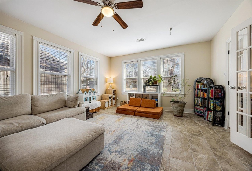 Spacious room featuring multiple windows, neutral wall tones, tile flooring, a ceiling fan, and French doors
