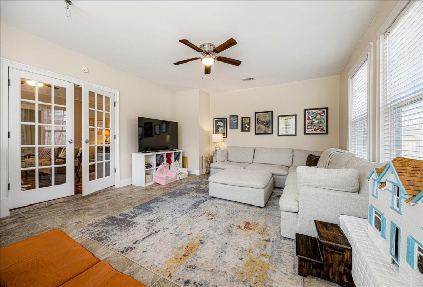 Spacious living area featuring tile flooring, French doors, a ceiling fan, and multiple windows with blinds