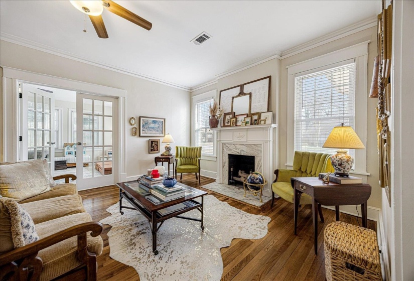 Hardwood flooring extends throughout this living space, featuring a white mantle fireplace with a marble surround and hearth