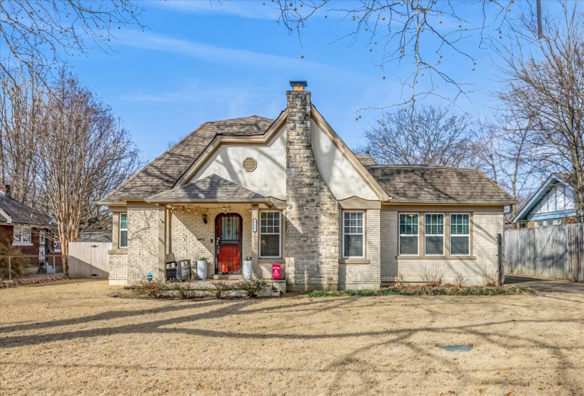 Charming brick and stone exterior featuring a prominent stone chimney, gabled roofline, and an inviting covered porch