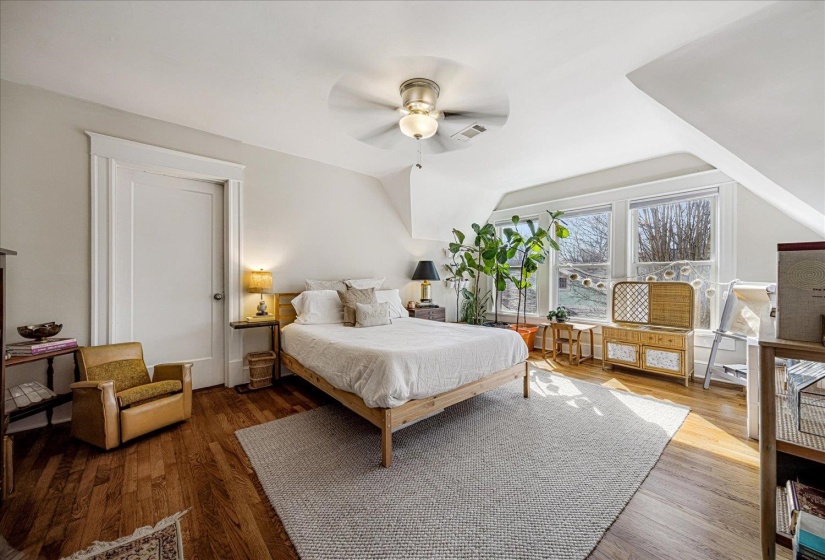 Hardwood flooring throughout this room featuring a ceiling fan, white trim, and ample natural light from multiple windows