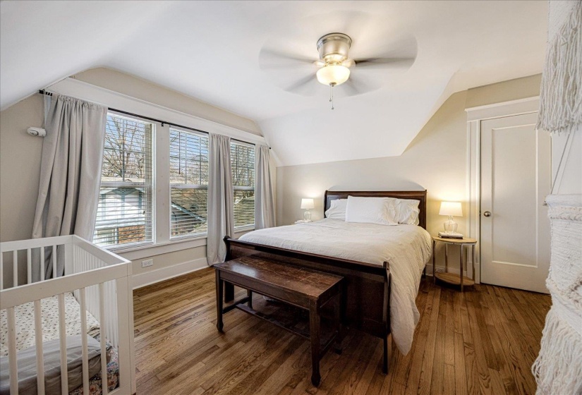 Bedroom featuring wood-finish flooring, a ceiling fan with integrated lighting, and multiple windows with blinds