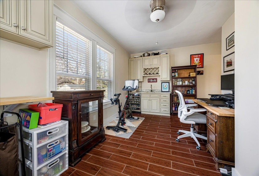Spacious multi-purpose room featuring wood-finish flooring, ample natural light from multiple windows, and a built-in wet bar with cabinetry