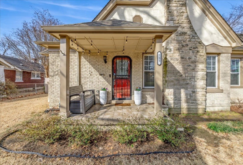 Inviting front entrance featuring a covered porch, a bold red front door with an ornate security screen, and a stone-clad chimney