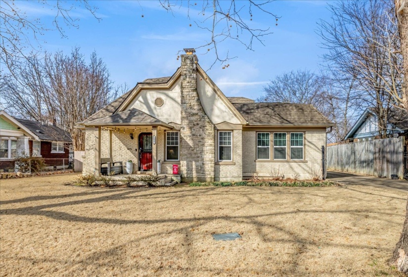 Tudor-style residence featuring a prominent stone chimney and a covered front porch with a red entry door