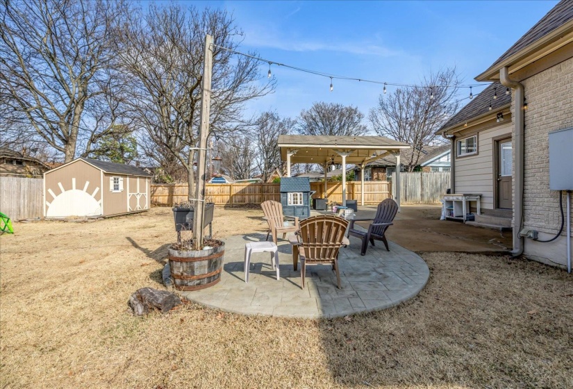 Expansive backyard featuring a circular stamped concrete patio, a detached storage shed, and a covered outdoor structure