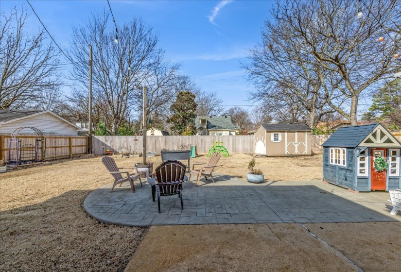 Expansive backyard featuring a curved stamped concrete patio, a wooden privacy fence, and a storage shed