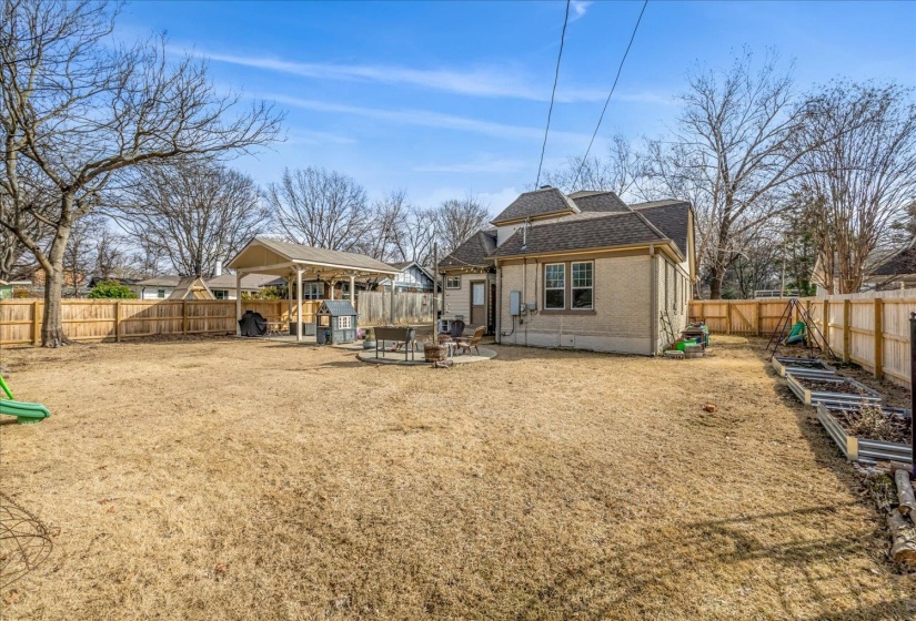 Expansive backyard featuring a privacy fence, covered patio structure, and raised garden beds