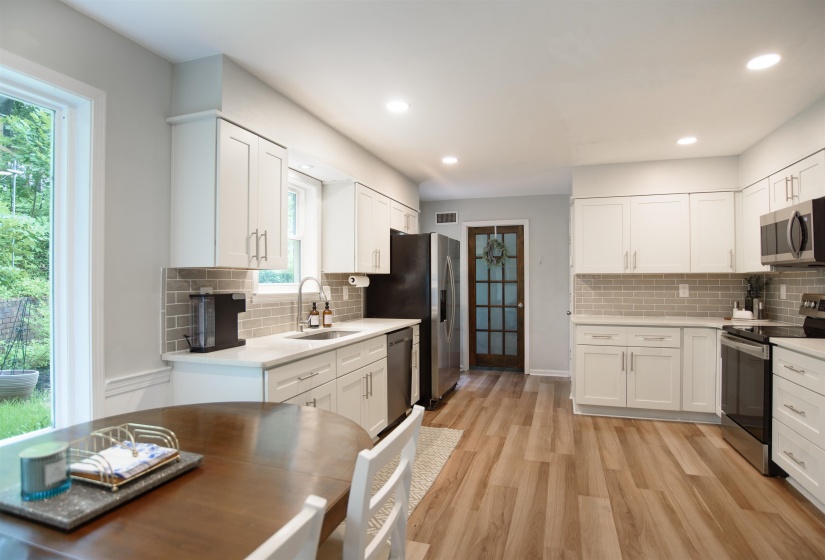 Kitchen featuring white cabinetry, light-toned countertops, a subway tile backsplash, stainless steel appliances, and wood-finish flooring