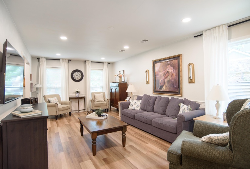 Spacious interior featuring wood-finish flooring, recessed lighting, crown molding, and multiple windows with white blinds and drapes