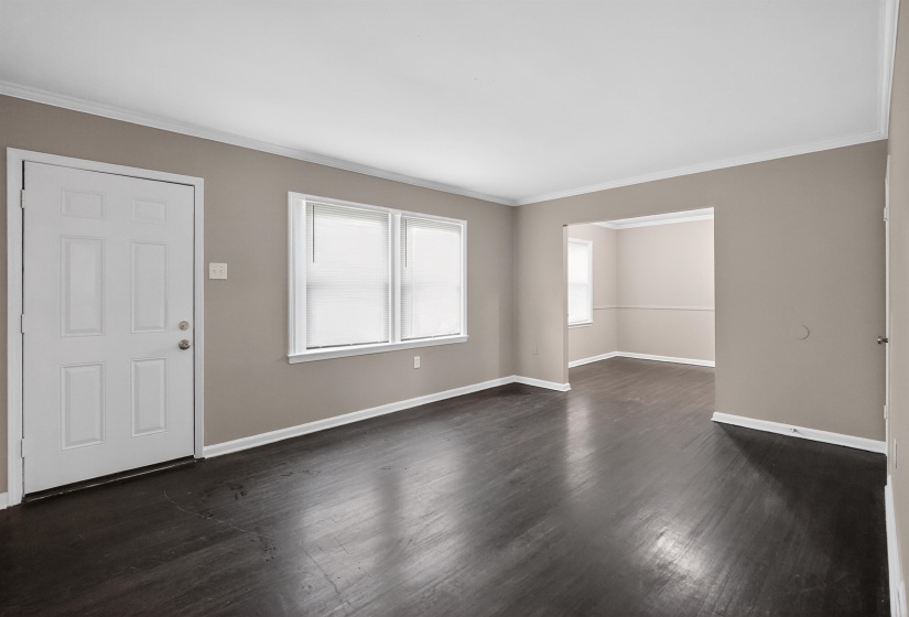 Spacious room with dark wood-finish flooring, light tan walls, and white trim