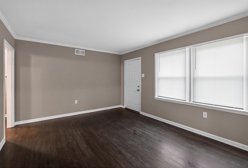 Spacious room featuring dark wood-finish flooring, neutral wall paint, and crisp white baseboards and crown molding