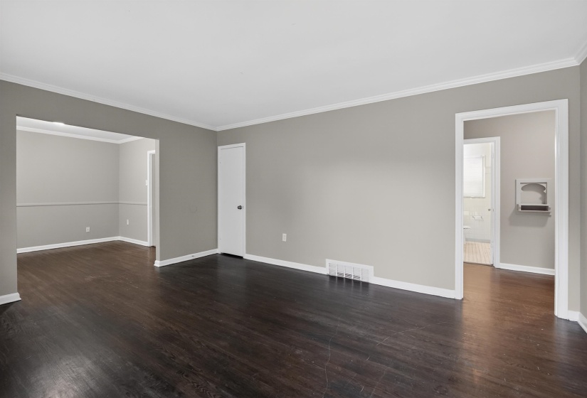 Spacious interior room featuring dark wood-finish flooring, light gray walls, and white crown molding