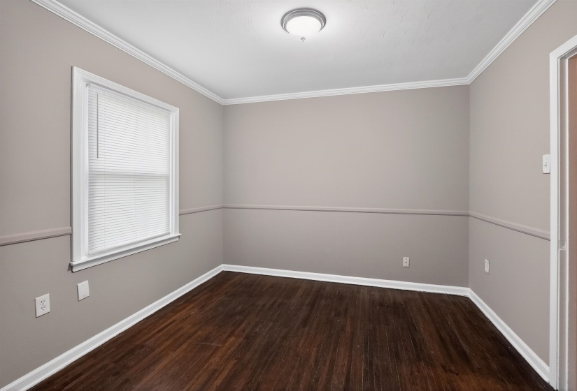 Room with wood-finish flooring, neutral gray walls, white crown molding, and white baseboards