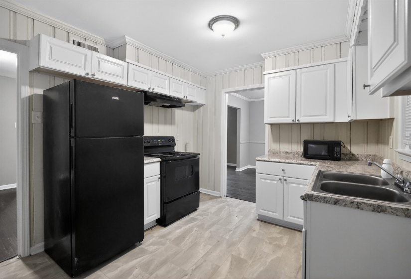 Kitchen featuring light-toned flooring, white upper and lower cabinetry, a black gas range, a black refrigerator, and a double basin stainless steel sink