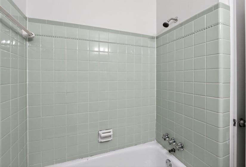 Bathtub with light green square tile surround, chrome fixtures, and a showerhead
