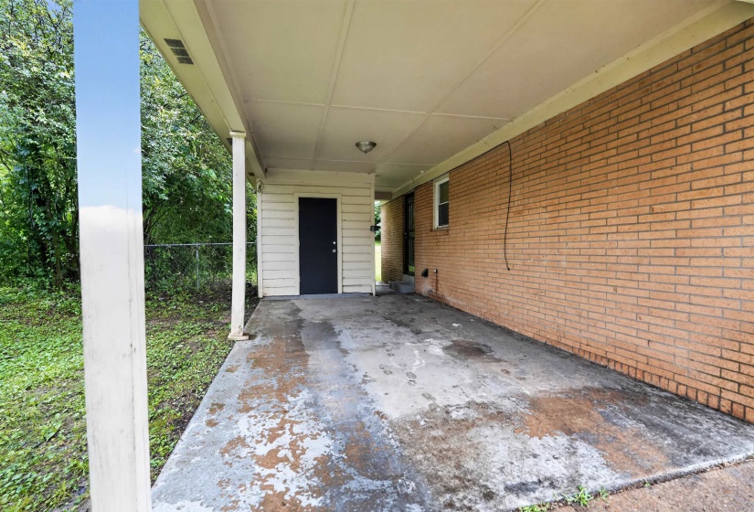 Covered concrete carport featuring a brick exterior wall, recessed lighting, and an exterior storage room with a black door