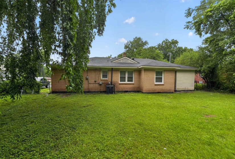 Spacious rear yard with a tan brick exterior, multiple windows, and a side-facing garage door