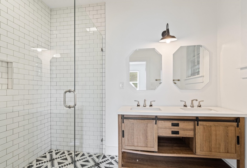 Bathroom featuring a glass-enclosed shower with white subway tile, patterned floor tile, a dual vanity with a light wood-finish cabinet, and two octagonal mirrors