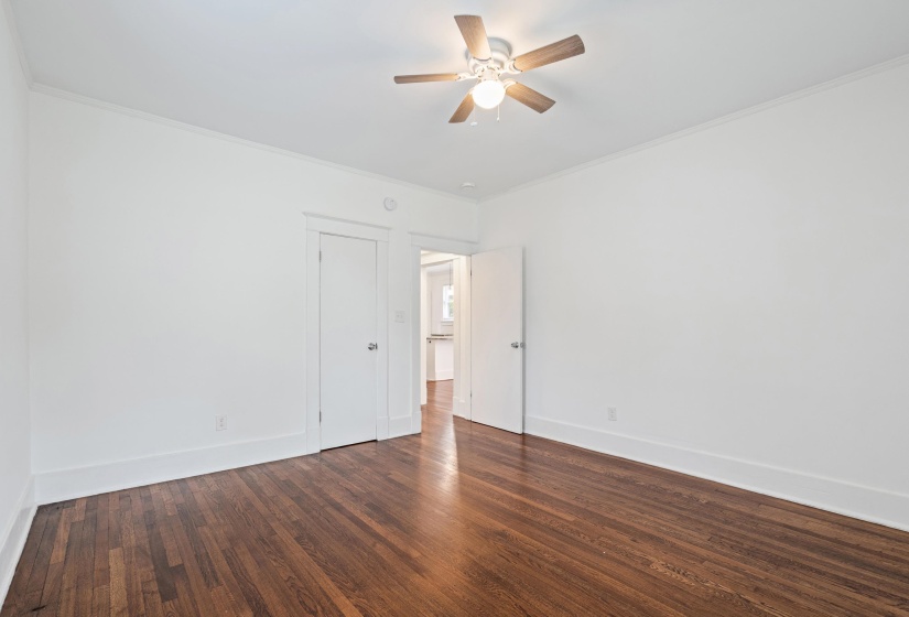 Spacious room featuring rich wood-finish flooring, crisp white walls, and a ceiling fan with integrated lighting
