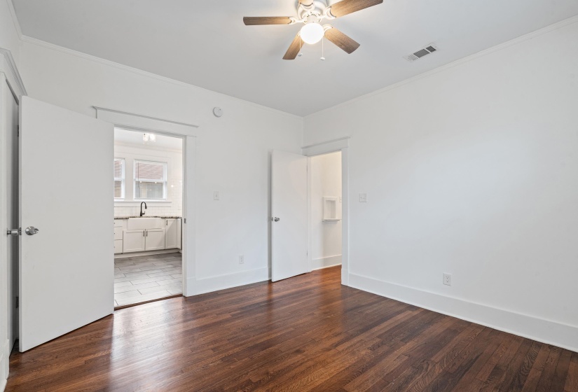 Spacious room with rich wood-finish flooring, a ceiling fan with light fixture, and crown molding
