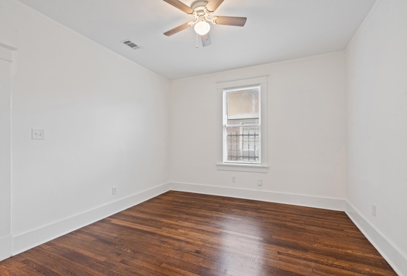 Interior room featuring rich wood-finish flooring, white walls, and a window with security bars