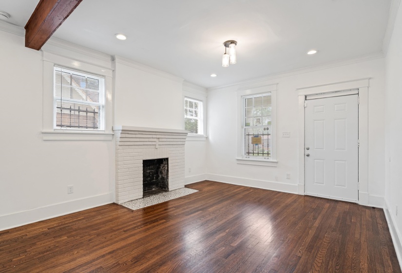 Hardwood flooring throughout featuring a white brick fireplace with a mosaic tile hearth
