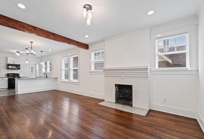 Hardwood flooring throughout the main living area, featuring a white painted brick fireplace with a patterned tile hearth