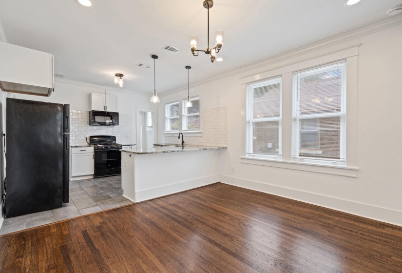Open-concept kitchen and living area featuring wood-finish flooring, white cabinetry, a subway tile backsplash, and a breakfast bar with a stone countertop
