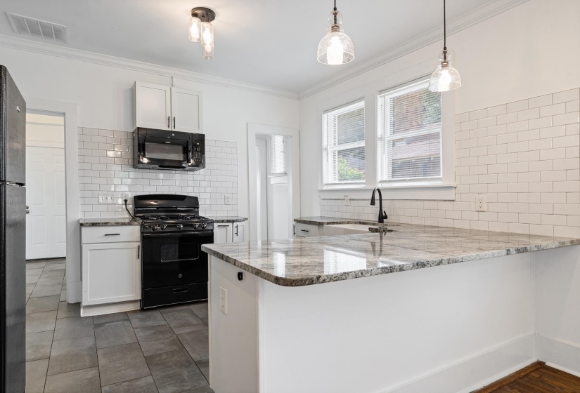Kitchen featuring an island with a stone countertop, white shaker cabinetry, subway tile backsplash, and stainless steel appliances including an oven range and microwave