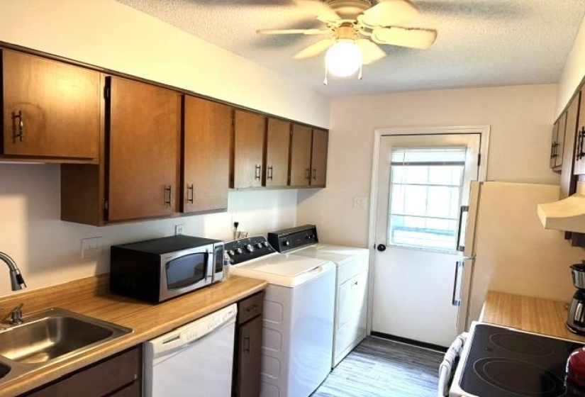 Kitchen area featuring wood-finish cabinetry, laminate countertops, a stainless steel sink, and wood-look flooring