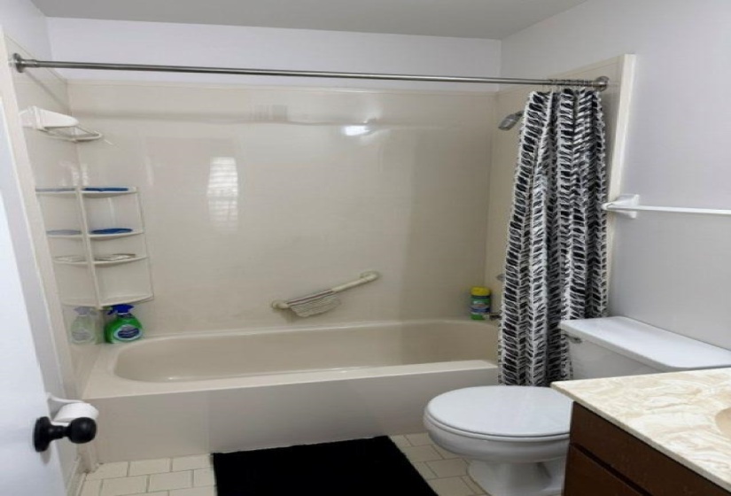 Bathroom featuring a combined tub and shower unit, a toilet, a vanity with a light-colored countertop, and light-toned floor tiles