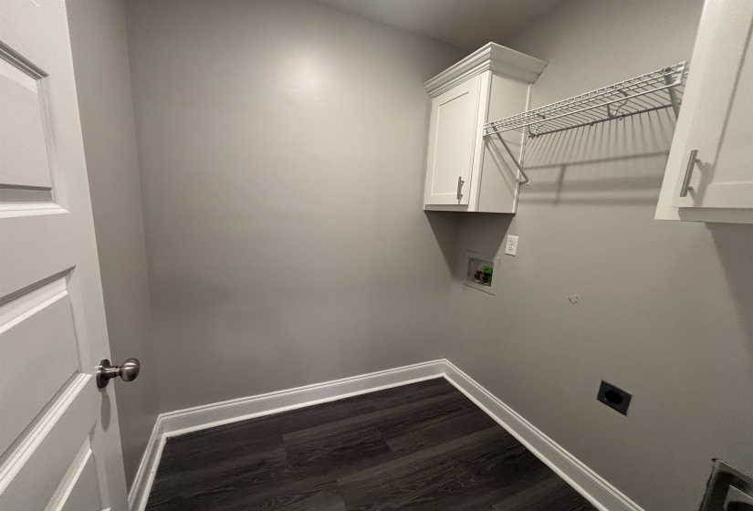 Laundry area with dark wood-finish flooring, light gray walls, white baseboards, and white cabinetry