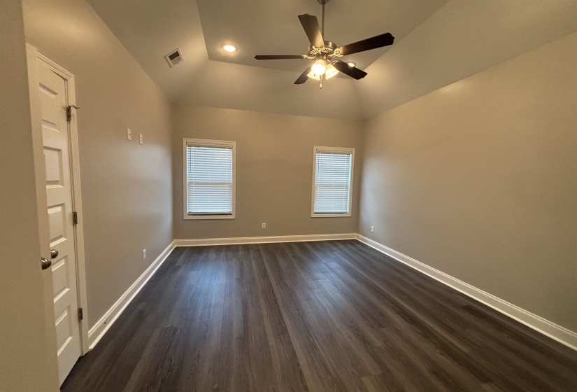 Spacious room featuring wood-finish flooring, a tray ceiling with recessed lighting, and a ceiling fan with light fixture